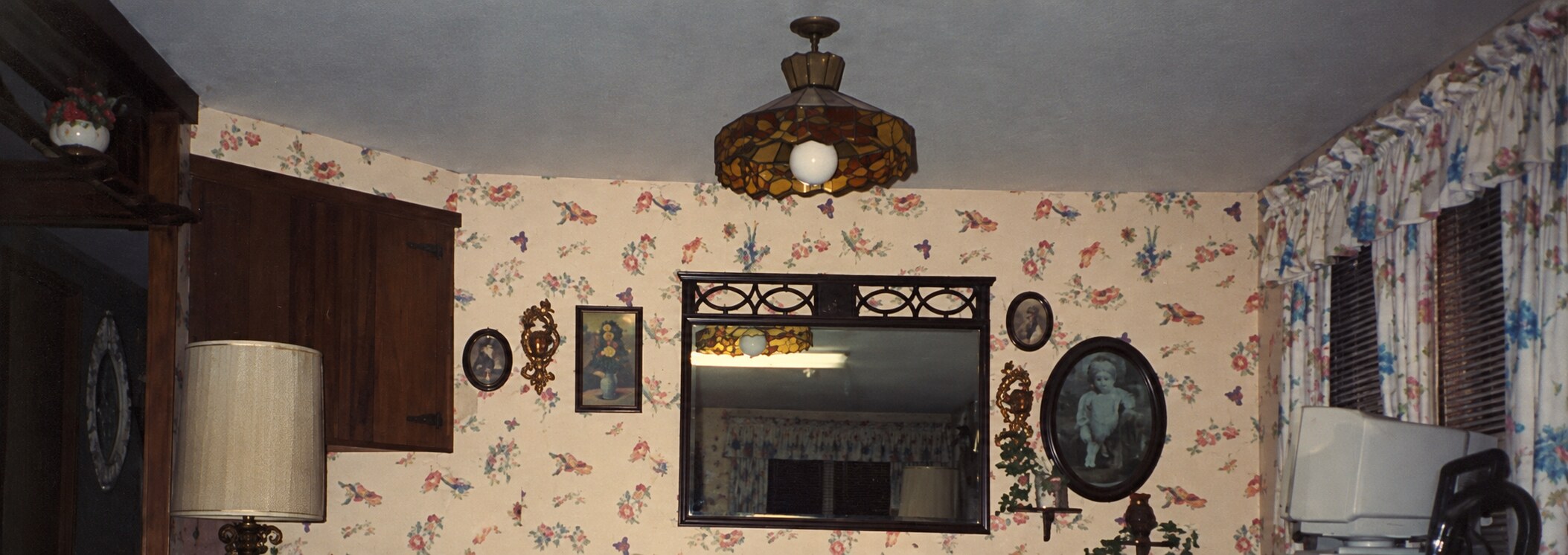 A restored detail of the trailer interior with floral wallpaper, framed pictures, mirrors, and a stained-glass ceiling light.