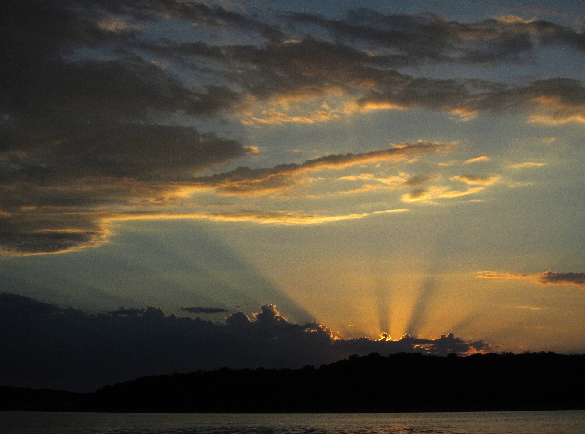 Golden light breaking through layered clouds above Beaver Lake at sunset